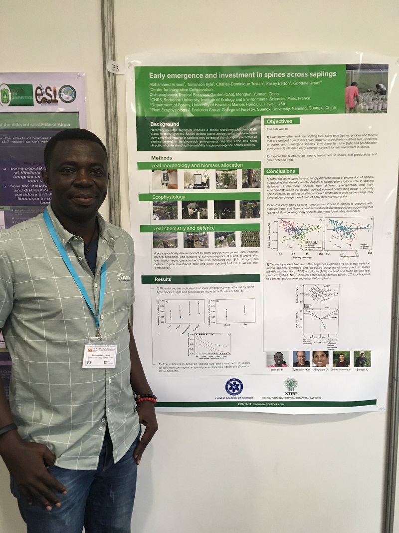 Poster prize winner Mohammed Armani smiling and standing in front of the winning poster hung on the wall.